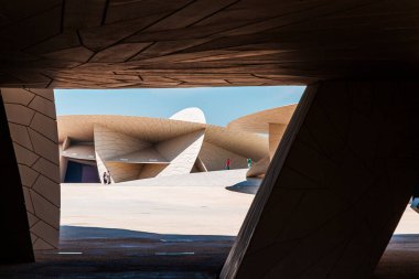 Katar Ulusal Müzesi, Doha, Katar: 15 Mart 2025. Katar Ulusal Müzesi 'nin çarpıcı bir çağdaş mimari sahnesi açısal beton formlar ve güneşli bir çöl ortamında geniş açık alanlar içeriyor. İnsanlar heykeli keşfeder.