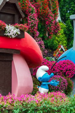 Dubai, Birleşik Arap Emirlikleri, BAE - 27 Mart 2024: Dubai Mucize Bahçesi, Dubai 'deki en popüler turistik merkezlerden biri. Büyük boy pembe ve kırmızı mantar şekilli mavi bir Şirin figürünün yer aldığı tuhaf bir bahçe görüntüsü. Mantar Şirinleri.