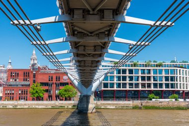Londra, İngiltere: 11 Mayıs 2025. Büyük bir kablo olan Millennium Köprüsü 'nün altından çekilen çarpıcı şehir sahnesi çelik iskeleti Thames Nehri' ni ve kırmızı tuğla tarihi binalar ile çağdaş cam ofis bloğu arasındaki zıtlığı gözler önüne seriyor.