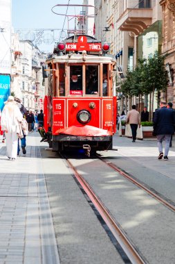 Istanbul, Turkey. April 15, 2022: A bright red vintage nostalgic tram on Istiklal Avenue glides along a crowded city street, surrounded by pedestrians and historic buildings. The scene captures urban life, travel, and iconic public transport in a liv