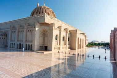 Sultan Qaboos Ulu Camii, Muscat, Umman - 31 Aralık 2023: Görkemli beyaz mermer cami büyük bir kubbe, kemerli girişler ve karmaşık taş işçiliği. Yansıtıcı mermer avlu ve mavi gökyüzü dinginlik, maneviyat ve mimarlık iletir
