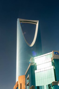 Riyad, Suudi Arabistan - 1 Ocak 2026: Riyad 'daki Krallık Merkezi, çağdaş otel mimarisinin üzerinde yükseliyor. Yelken şeklindeki cam kule, parlak gün ışığını yansıtır. Derin mavi gökyüzüne karşı, lüks tasarım ve modern urb sergilenir.