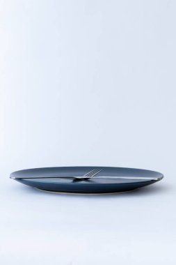 Beyaz zemin üzerinde paslanmaz çelik çatal ve bıçak olan mavi seramik tabak. Asgari sofra takımı ve yemek teması.