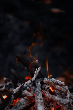 Gece kamp ateşinde parlayan alevlerin ve yanan odunların yakın çekim görüntüsü. Sıcak ışık, kıvılcımlar ve detaylı ateş dokusu sıcak ve büyüleyici bir atmosfer yaratır..
