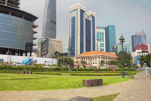 Busy street traffic with motorbikes passing in front of a historic colonial building and modern skyscrapers in downtown Ho Chi Minh City, Vietnam. A vibrant urban lifestyle scene in Southeast Asia.
