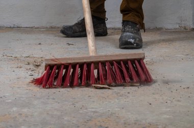Kırmızı tüylü süpürgeyle tozlu bir zemini süpüren kişi.