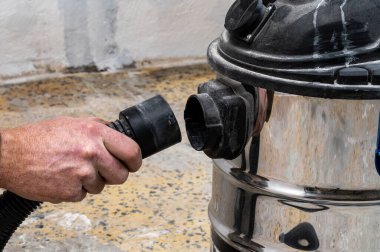 Hortumu ıslak-kuru elektrik süpürgesine bağlayan kişi.