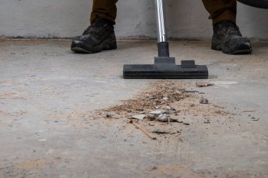 Beton zeminde elektrikli süpürgeyle döküntü süpüren biri..