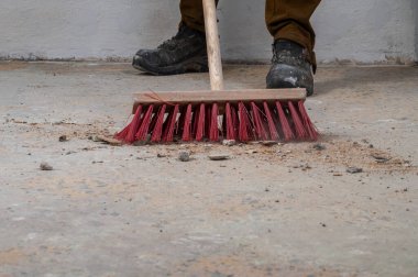 Kırmızı süpürgeyle tozlu zemini süpüren kişi.