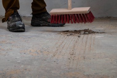 Kırmızı süpürgeyle beton zemini süpüren kişi..