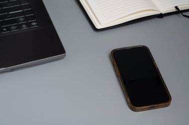 Akıllı telefon, dizüstü bilgisayar ve gri bir masada açık bir defter..