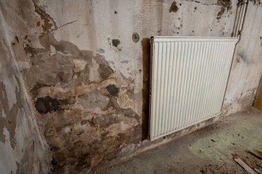 Nemli, küflü bir duvarda çürüyen bir odada eski radyatör..