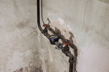 Beton duvarda paslı borular ve vanalar olan eski su sayacı..