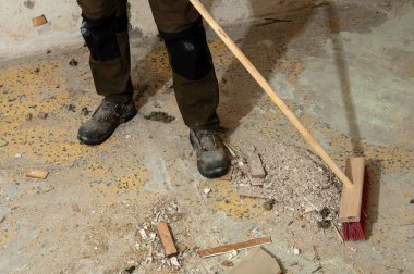 Tadilat sırasında beton zemindeki enkazı süpüren inşaat işçisi. El işçiliği, iş güvenliği, endüstriyel temizlik ve inşaat sonrası bakım kavramı