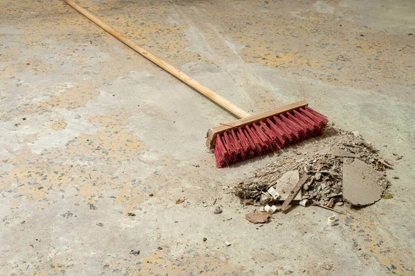 Temizlik sırasında beton zeminde inşaat enkazı toplayan süpürge. El işi, bakım, işyeri temizliği ve inşaat sonrası temizlik kavramı