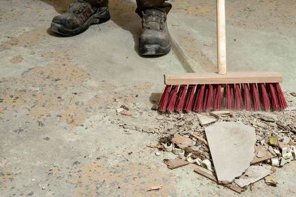 Beton zemindeki süpürge ve güvenlik botlarıyla inşaat temizliği sürüyor. Tadilat alanında iş güvenliği, el emeği, endüstriyel temizlik ve inşaat sonrası bakım kavramı