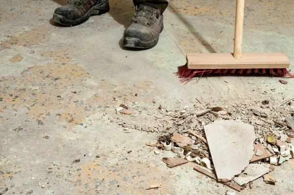 İnşaat işçisi bir yenileme alanının beton zeminini süpürüyor. El işçiliği, iş güvenliği, endüstriyel temizlik, inşaat sonrası temizlik ve bina bakımı kavramı