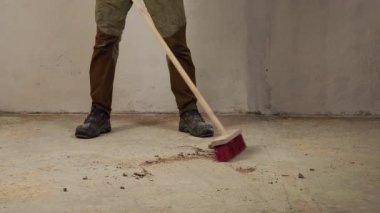 Temizlik sırasında beton zemini süpüren bir işçi. İnşaat ve yenilenmeden sonra tozu ve enkazı elle temizleme işlemi. Ev geliştirme ve inşaat bakım kavramı