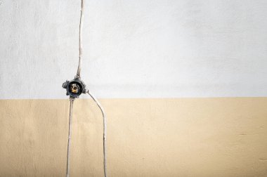 Beton bir duvara monte edilmiş asgari elektrik bağlantı kutusu, basit bir faydacı kompozisyonda açık kablolar ve endüstriyel detaylar içeriyor.