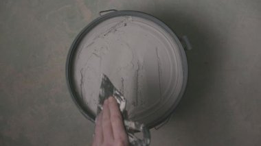 Elinde malayla açık kovadan alçı çıkartan el temizleme alçısının yukarıdan görünüşü, iç inşaat ve duvar hazırlıkları sırasında hassas bir yenileme adımını gösteriyor.