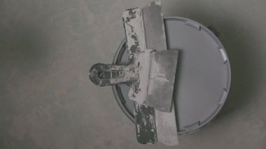 Kova kapağından alçı aletlerini çıkartan bir elin yukarıdan görünüşü, temiz ve minimal bir inşaat ortamında hazırlıktan aktif yenileme çalışmasına geçiş.