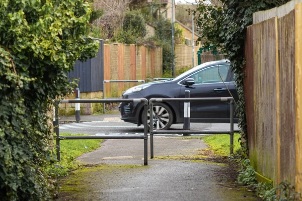 Metal bariyerlerle dolu dar bir patikadan geçen araba.