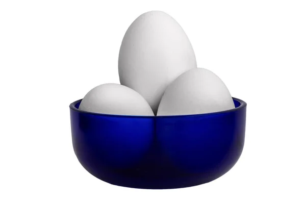 Beyaz arka planda izole edilmiş mavi bir seramik kasede üç beyaz tavuk yumurtası. Küçük stüdyo hayatı, yemek konsepti, yemek malzemeleri, kahvaltı ve sağlıklı beslenme.