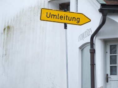 Beyaz duvarlı ve eski yosunlu alçılı bir antikacının önündeki işaret..