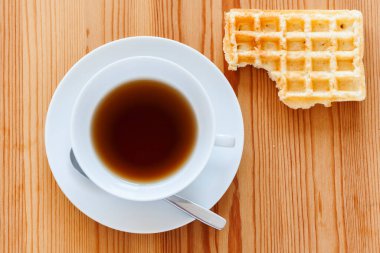 Tabağı ve kaşığı olan ahşap bir masa yanı sıra üzerinde ısırık izi olan bir waffle..
