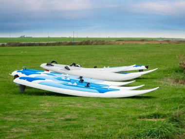 2020 sonbaharında Doğu Frizya / Almanya 'da bulutlu bir gökyüzü olan yeşil bir çayırda mavi ve beyaz sörf tahtaları depolandı.. 