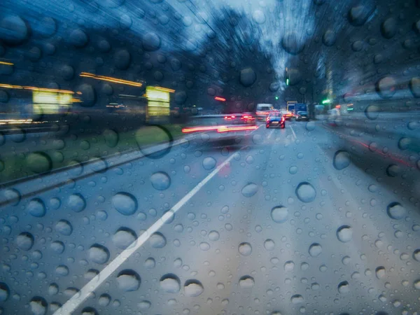 Şafak vakti ıslak bir şehir caddesinde uzun süre yol trafiği görüldü. Yağmur damlalı bir sürücünün perspektifinden.. 