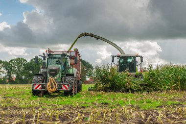 Esens, Almanya - 07 Ekim 2020: Mısır helikopteri ve traktörden oluşan mısır hasatçıları yoğun bulutlu bir gökyüzü altında devrilen römork.