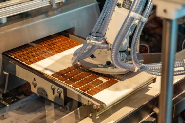 Robotik kol, sertleştirilmiş çikolata, mekanik tutucu hareket halindeki kemer, sensörler ve servo parçaları görünür hale getiriyor, yüksek teknoloji otomasyon hızı ve tutarlılığı artırıyor.