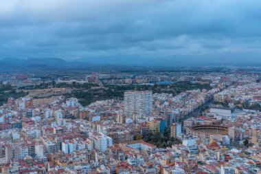 Şehrin bulutlu hava manzarası, çatıları ve dar caddeleri olan yoğun konut blokları, inşaat vinçleri ve dağınık yükseklikler, kentsel yoğunluğu ve gelişimi aktaran sessiz renk paleti