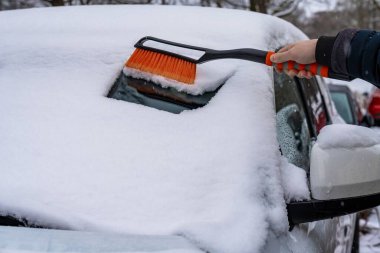 El, portakal fırçasını hızla ön camdan kaldırıyor. Kalın tabakayı temizliyor. Eldivenli tutuş, güvenli sürüş için görünürlüğü arttırıyor..