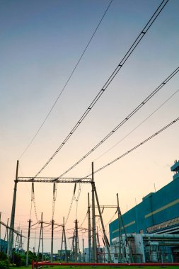 Elektrik şebekesi altyapısının büyüleyici görüntüsü sanayi bölgesinde alacakaranlık gökyüzünün arkaplanına karşı. Görüntü, elektrik iletiminin özünü yakalar ve...