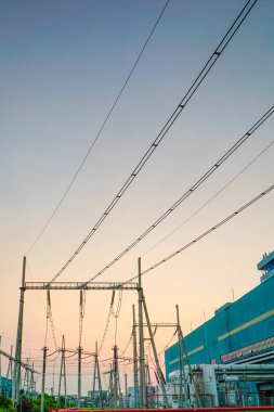 Bir elektrik şebekesinin siluetinin alacakaranlıkta kaybolan ışığa karşı görüntüsünü gösteren çarpıcı bir görüntü. Bu sahne modern enerji kaynağımızı destekleyen endüstriyel mahareti özetliyor.,