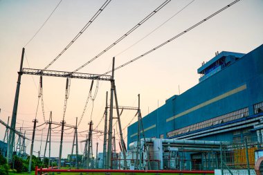 Alacakaranlıkta bir elektrik santrali ve elektrik şebekesinin görüntüsü günbatımı gökyüzüne karşı endüstriyel altyapı ve enerji iletim sistemlerini vurguluyor.