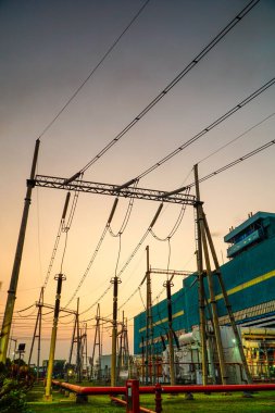 Bir elektrik santralinin şebeke altyapısının silueti sessiz ve karanlık bir gökyüzüne karşı yakalanır. Yüksek voltajlı elektrik hatları elektrik enerjisi taşıyan karmaşık bir ağ oluşturuyor.,