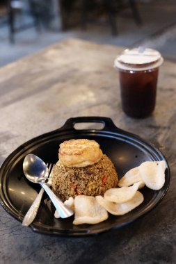 Lezzetli bir kızarmış pirinç yemeği, çıtır krakerler ve enfes bir mutfak deneyimi için ferahlatıcı bir çay içeceği ile tamamlanmış şeffaf siyah bir tepside sunulur. Yemek blogları için mükemmel bir görüntü.