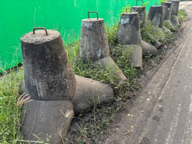 Metal saplı beton bariyerler yeşil zemin duvarlı bir yolun kenarında duruyor.