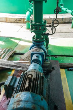 Daha yakından bakınca endüstriyel bir pompa sisteminin karmaşık detaylarını gösteriyor. Görüntü, makinelerin karmaşıklığını ortaya çıkaran yeşil borular ve mavi motorun bir kombinasyonunu içeriyor..