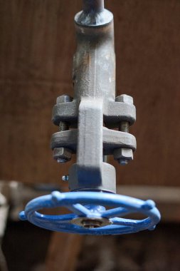 Eski endüstriyel bir valfın detaylı bir yakın çekimi metalik yapısını ve tekerleğinin parlak mavisini vurguluyor. Kapakçık yıpranmış görünüyor. Yaşını ve önemini gösteriyor.