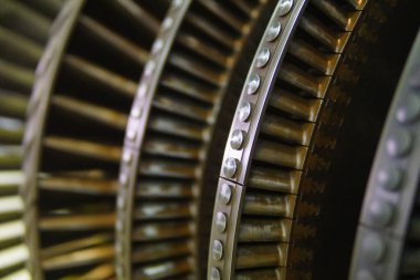 Mühendislik ve mekanik tasarım elementlerini vurgulayan bir türbin pervanesinin karmaşık yakın çekimi. Enerji için endüstriyel makineler içindeki karmaşık metaller vasıtasıyla güç üretimi gösteriliyor