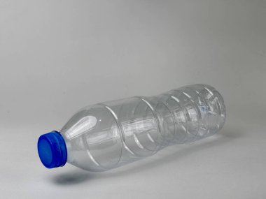 Mavi kapaklı, temiz bir yüzeye yatay dinlenen boş, temiz bir plastik şişe. Şişenin şeffaflığı geri dönüşüm ve çevre bilinci kavramını vurguluyor.