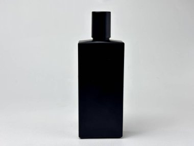 Minimalist bir stüdyo çekiminde kozmetik veya parfüm ürünlerini sergilemek için ideal bir siyah mat şişesi bulunur. Şişenin temiz geometrik tasarımı düz beyaz bir zemine karşı duruyor..