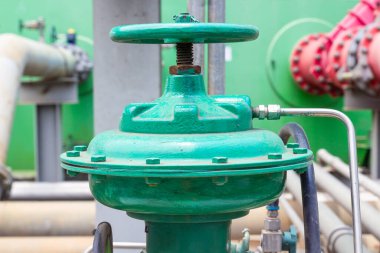 Yakın çekim, fabrikada ya da fabrikada eşlik eden bir boru ile endüstriyel yeşil bir vana yakalıyor. Fotoğraf kapakçığın sağlam yapısını ve karmaşık bağlantılarını vurguluyor.,