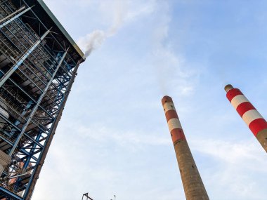 Gökyüzüne karşı bacaların ve yapısal çelik iskeletin yer aldığı dramatik sanayi manzarası
