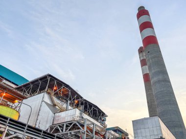 Bir elektrik santralinin uzun, kırmızı ve beyaz çizgili bacalarının soluk gökyüzüne çarpan görüntüsü..