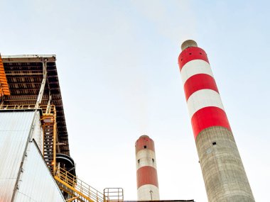 Endüstriyel bacalar parlak bir gökyüzünün altında yükseliyor, kırmızı ve beyaz çizgili tasarımı sergiliyor.